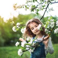 A cute little girl of 5 years old in a blooming white apple orchard in spring. Springtime, orchard, flowering, allergy, spring fragrance, tenderness, caring for nature. Portrait photo