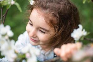 una linda niña de 5 años en un floreciente huerto de manzanas blancas en primavera. primavera, huerta, floración, alergia, fragancia primaveral, ternura, cuidado de la naturaleza. retrato foto