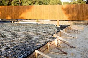 Iron fittings on a wooden formwork with laid pipes are the basis for pouring the foundation of the house with a concrete slab. Construction of cottages, design, engineering communications. photo