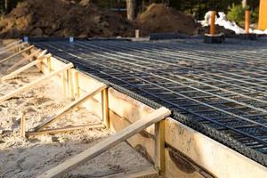 Iron fittings on a wooden formwork with laid pipes are the basis for pouring the foundation of the house with a concrete slab. Construction of cottages, design, engineering communications. photo