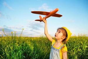 Girl in a yellow panama hat launches a toy plane into the field. Summer time, happy childhood, dreams and carelessness. Air tour from a travel agency on a trip, flight, adventure and vacation. photo