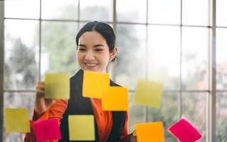 Business asian woman use message paper stick on glass board with window light. photo