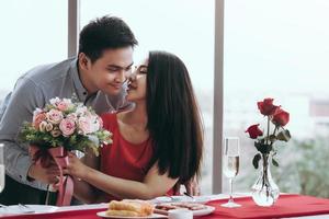 pareja asiática con ramo de flores en la mesa de la cena en san valentín. foto