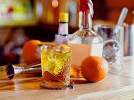 Old fashioned cocktail, orange, bottles and beaker on the bar counter