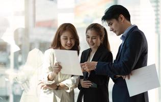 Group of businesspeople using a report together in front of office building windows overlooking the city photo