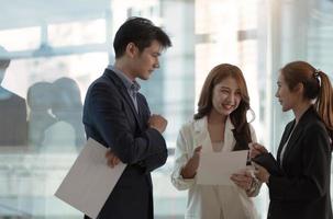 Group of businesspeople using a paper together in front of office building windows overlooking the city photo