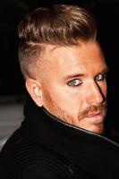 Portrait of a fashionable young man with blue eyes, stylish haircut and posing with a black jacket. Close up. Vertical image. photo