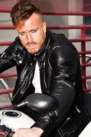 Trendy young man with black leather jacket on a motorcycle with a defiant look. Vertical image. photo