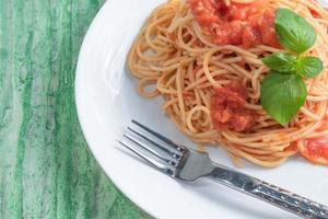 Pasta with tomato sauce in white dish on green wood background