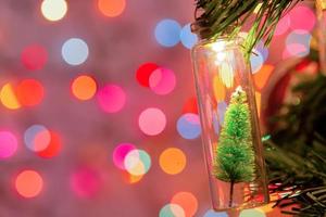 Merry Christmas and happy new year. Hanging small Christmas tree in glass jar on pine branches Christmas tree garland and ornaments over abstract bokeh photo