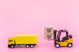 logística y servicio de entrega: camión de carga, carretilla elevadora y cajas de papel o paquetes con el logotipo de un carrito de la compra sobre fondo rosa. servicio de compra en la web online y ofrece servicio a domicilio.
