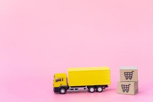 logística y servicio de entrega: camión de carga y cajas de papel o paquetes con el logotipo de un carrito de la compra sobre fondo rosa. servicio de compra en la web online y ofrece servicio a domicilio. foto