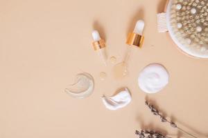 Smears and drops of various cosmetic products top view and pipettes on beige background with dry lavender. Flat lay photo