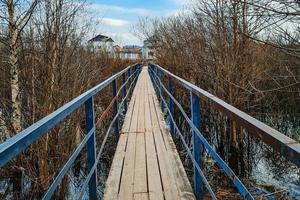 Old wooden bridge over the river in village. Narrow pedestrian crossing. photo
