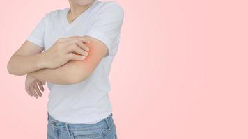 mujer joven rascándose el codo en el fondo de la pared rosa. foto