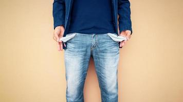 Man showing his empty pockets on cement wall background. photo