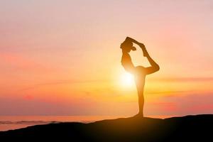 silueta de mujer joven con sendero recortado practicando yoga ejercicio relajante en la cima de la montaña puesta de sol en la playa foto