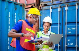 Worker man in hardhat and safety vest holding clipboard checklist and Female foreman using laptop control loading containers box from cargo photo