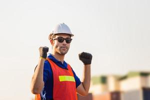 Factory worker man in hard hat with celebrating victory, young man celebrates with two hand in the air