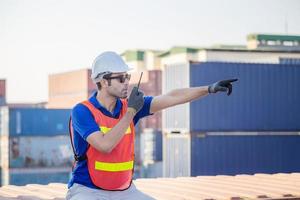 Foreman in hardhat and safety vest talks on two-way radio control loading containers box from cargo photo