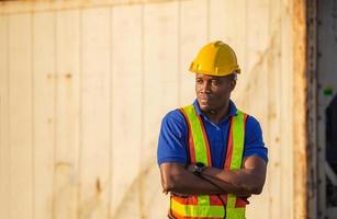 Cheerful factory worker man in hard hat smiling with arms crossed as sign of success blurred container box background photo