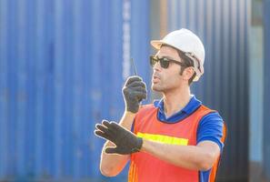 Foreman in hardhat and safety vest talks on two-way radio control loading containers box from cargo photo