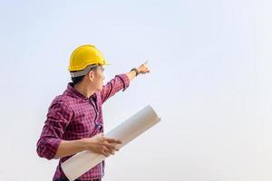 hombre ingeniero revisando y planificando el proyecto en el sitio de construcción, hombre sosteniendo un plano y apuntando al cielo foto