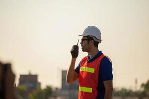 Foreman worker in hardhat and safety vest talks on two-way radio control loading containers box from cargo photo