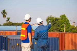 Worker man in hardhat and safety vest and foreman checking control loading containers box from cargo, Teamwork concepts photo