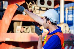 Foreman in hardhat and safety vest talks on two-way radio control loading containers box from cargo photo