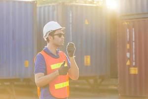 Foreman in hardhat and safety vest talks on two-way radio, Factory worker control loading containers box from cargo photo