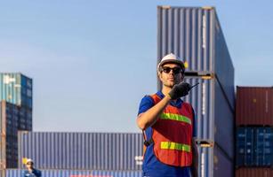 ingeniero en casco y chaleco de seguridad con radio bidireccional, equipo de trabajadores de fábrica en contenedor de carga foto