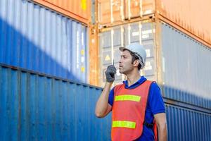 Foreman in hardhat and safety vest talks on two-way radio control loading containers box from cargo photo