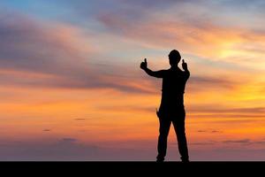 Silhouette of Factory worker man with clipping path in hard hat with thumbs up, young man celebrates with hand in the air sunset background photo