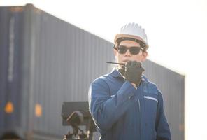 Foreman in hardhat and safety vest talks on two-way radio control loading containers box from cargo photo