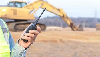 Civil engineer holding a radio with an excavator in the background photo