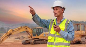 A middle-aged engineer uses a walkie-talkie on the work site, an Asian elder supervises the evening work. photo