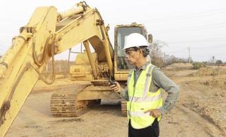 ingeniero senior con transmisor de radio portátil en el fondo de la excavadora foto