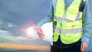 Engineer holding hard hat with walkie-talkie on sky background photo