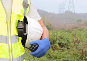 Hand holding a radio transmitter or the arm of an engineer or worker holding onto a white helmet. Prepare for work safety photo