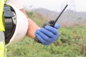 mano sosteniendo un transmisor de radio o el brazo de un ingeniero o trabajador sosteniendo un casco blanco. prepararse para la seguridad en el trabajo foto