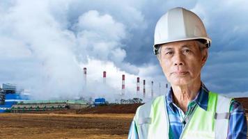 Senior Asian engineer wearing helmet and safety vest against power plant or factory background. photo