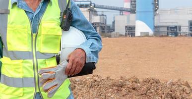 Engineer or worker holding helmet and work gloves against factory background photo