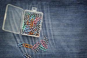 Set of colorful paperclips in plastic box on jeans background photo