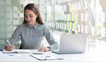 Mujer de negocios que usa la calculadora para hacer finanzas matemáticas en un escritorio de madera en la oficina y el fondo de trabajo empresarial, impuestos, contabilidad, estadísticas y concepto de investigación analítica foto