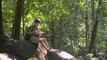 Female naturalist working on digital tablet while sitting on the rock in tropical forest. video