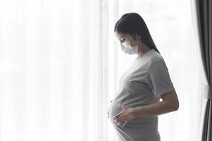 Young pregnant woman wearing a protective mask and expecting a baby, healthy and motherhood concept photo