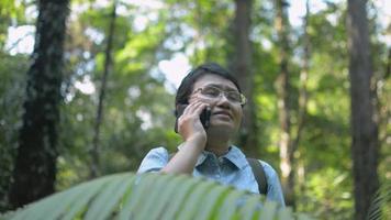 mulher bonita asiática com mochila falando no celular na floresta tropical.