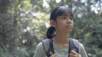 Pretty teenage girl with backpack looking around among tropical rainforest during summer. video