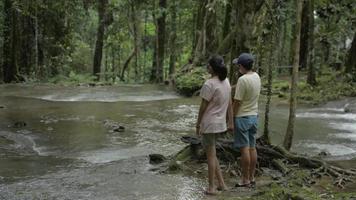 Mother and her teenager daughter enjoy with scenery of water stream in tropical rainforest.